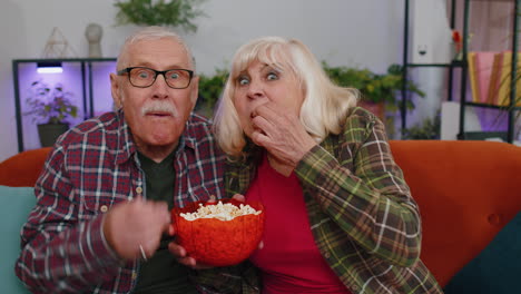 Senior-family-couple-grandparents-man-woman-watching-interesting-TV-football-movie,-eating-popcorn