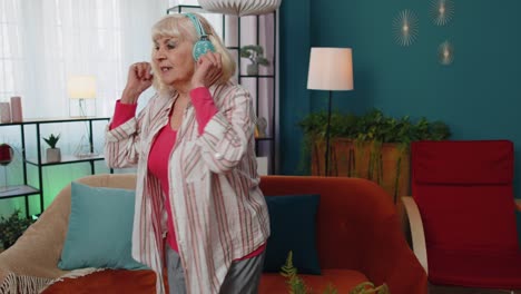 Überglückliche-ältere-Frau-Mit-Kabellosen-Kopfhörern,-Die-Auf-Einer-Gemütlichen-Couch-Im-Wohnzimmer-Zu-Hause-Tanzt-Und-Singt