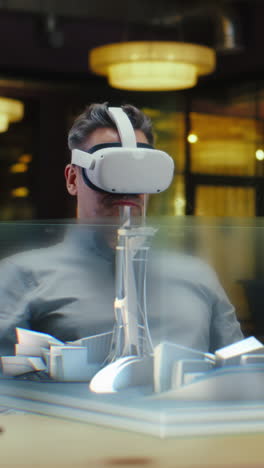 Male-architect-uses-VR-headset-and-wireless-controllers,-creates-architectural-project-of-metropolis-in-virtual-reality.-Man-works-in-hi-tech-company.-3D-hologram.-Vertical-shot