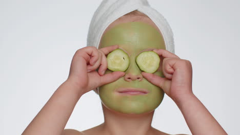 Schönes-Lächelndes-Kind-Mit-Handtuch-Auf-Dem-Kopf,-Das-Eine-Reinigende,-Feuchtigkeitsspendende-Grüne-Maske-Auf-Das-Gesicht-Aufträgt