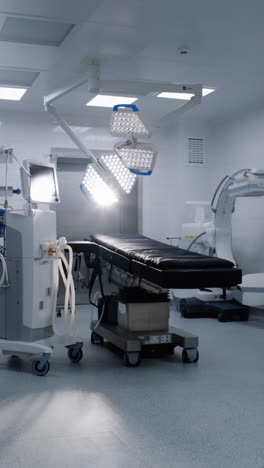 Vertical-shot-of-operating-room-in-modern-hospital-with-advanced-equipment-for-surgery.-Operating-table,-LED-lamps,-life-support-and-anesthesia-machine.-Operation-block-in-clinic-or-medical-facility.