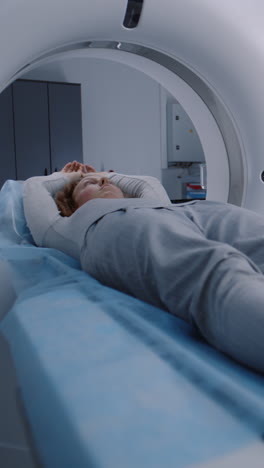 Vertical-shot-of-woman-lying-on-CT-or-PET-or-MRI-scan-bed-and-moving-inside-machine.-Scanning-of-patient-body-and-brain-using-high-tech-modern-equipment.-Medical-facility-with-advanced-technologies.