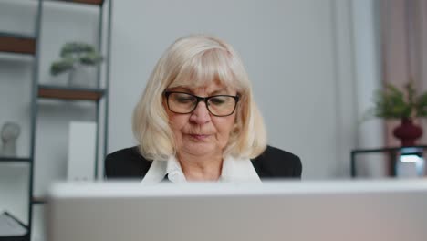 Senior-business-woman-freelancer-using-laptop-computer-sits-at-workplace-typing-browsing-at-office