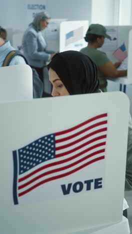 Mujer-árabe-Con-Hijab-Vota-En-La-Cabina-De-La-Oficina-De-La-Mesa-Electoral.-Día-De-Las-Elecciones-Nacionales-En-Estados-Unidos.-Carreras-Políticas-De-Los-Candidatos-Presidenciales-Estadounidenses.-Concepto-De-Deber-Cívico-Y-Patriotismo.-Tiro-Con-Plataforma-Rodante.