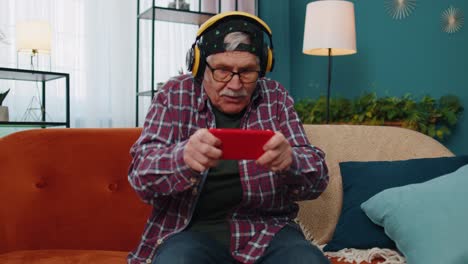 Worried-funny-senior-old-grandfather-man-playing-shooter-online-video-games-on-mobile-phone-at-home