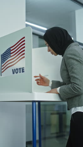 Una-Mujer-Musulmana-Con-Hijab-Viene-A-Votar-En-Una-Cabina-De-La-Oficina-De-La-Mesa-Electoral.-Día-De-Las-Elecciones-Nacionales-En-Los-Estados-Unidos.-Carreras-Políticas-De-Los-Candidatos-Presidenciales-Estadounidenses.-Concepto-De-Deber-Cívico.-Tiro-Con-Plataforma-Rodante.