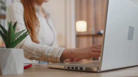 Mujer-Joven-Usando-Una-Computadora-Portátil-Sentada-En-La-Mesa-Trabajando,-Escribiendo-En-El-Teclado-Desde-La-Oficina-En-Casa