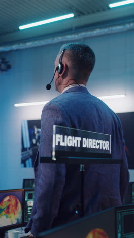 Vertical-shot-of-man-in-suit-pointing-at-screen-and-giving-commands-to-operators-during-launch-of-spacecraft-in-flight-control-center