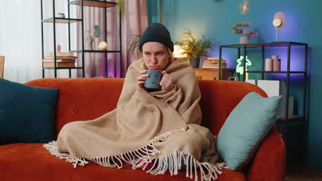 Ill-sick-unhealthy-woman-freezes-from-the-cold-feels-bad-covered-by-warm-blanket-drinks-tea-at-home