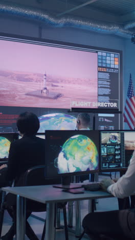 Boss-and-employees-watching-successful-launch-of-rocket-on-large-screen-then-applauding-and-giving-high-five-during-work-in-flight-control-center.-Vertical-shot