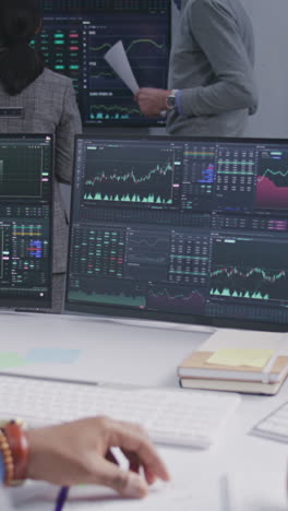 Financial-analyst-spins-pencil-in-hand,-works-in-bank-office.-Real-time-stocks,-exchange-market-charts-and-TV-news-displayed-on-computer-monitors.-Analytics-and-cryptocurrency-trading.-Vertical-shot