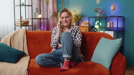 Smiling-young-Caucasian-woman-making-mobile-phone-conversation-with-friends-sitting-on-couch-at-home