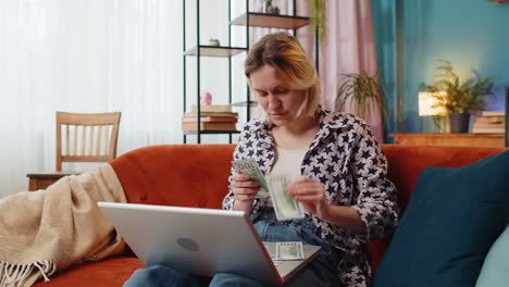 Rich-happy-young-woman-freelancer-counting-money-cash-use-laptop-computer-planning-home-budget