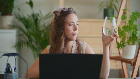 Inspired-Woman-Holding-Glass-of-Water-Working-Laptop-Window