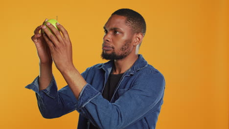 Male-model-examining-a-green-apple-to-be-clean-after-harvesting