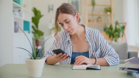 Woman-Browsing-Smartphone-While-Learning-at-Desk