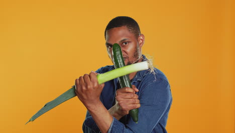 Pleased-young-adult-pretending-to-start-a-fight-with-a-cucumber-and-a-leek