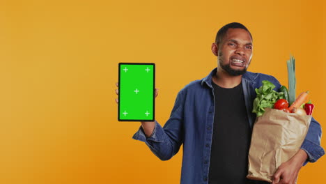 Vegan-adult-holding-a-tablet-with-greenscreen-layout-in-studio