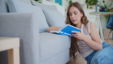 Woman-Focused-on-Reading-and-Studying-by-Sofa-on-Floor