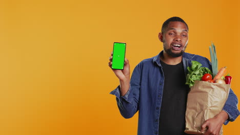 Young-adult-holding-a-smartphone-with-greenscreen-layout-in-studio