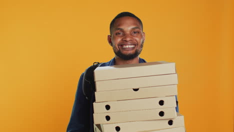 Male-pizzeria-courier-carrying-huge-pile-of-pizza-boxes-in-studio