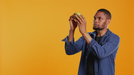 Male-model-examining-a-green-apple-to-be-clean-after-harvesting
