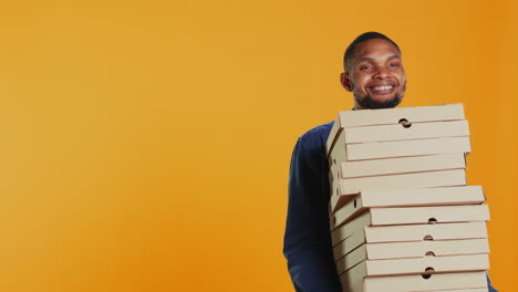 Selbstbewusster-Männlicher-Kurier-Trägt-Einen-Großen-Stapel-Pizzakartons,-Um-Eine-Fast-Food-Bestellung-Auszuliefern