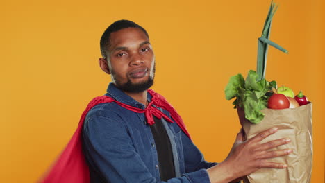 Young-adult-acting-as-a-superhero-with-a-red-cape-presenting-homegrown-produce