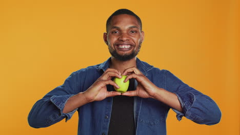 African-american-relaxed-guy-does-a-heart-shape-sign-with-an-apple