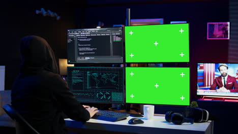 Hooded-man-writing-lines-of-code-on-green-screen-PC-from-apartment