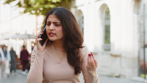 Angry-mad-stressed-Indian-young-woman-arguing-while-talking-on-smartphone-irritated-shout-quarrel