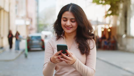 Indische-Frau-Nutzt-Smartphone,-Um-Textnachrichten-Zu-Tippen-Und-Im-Internet-Zu-Surfen,-Während-Sie-Ihre-Arbeit-Beendet-Und-In-Die-Kamera-Blickt