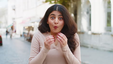 Indian-woman-looking-surprised-at-camera-shocked-by-sudden-win-good-victory-news,-wow-in-city-street
