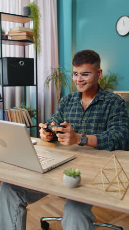 Excited-Indian-man-playing-video-game-on-laptop-computer-spending-leisure-time-at-home-office