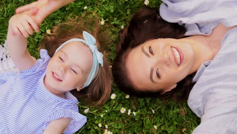 Happy-Mother-with-Baby-Girl-Lying-on-Grass-in-Park.family,-motherhood-and-people-concept-happy-smiling-mother-with-baby-girl-lying-on-grass-in-park