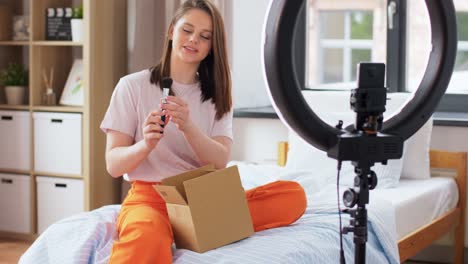 Happy-Girl-Blogger-Unpacking-Parcel-Box-at-Home.blogging,-technology-and-people-concept-happy-smiling-girl-or-beauty-blogger-with-ring-light-and-smartphone-unpacking-parcel-box-with-cosmetics-at-home