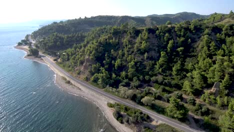 Luftaufnahme-Einer-Straße-Neben-Einem-Strand-Und-Unter-Einem-Hügeligen-Hügel-In-Griechenland