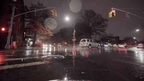Ein-Auto-Fährt-Nachts-Durch-Eine-Regenpfütze-In-Der-Stadt-Und-Ein-Auto-Fährt-über-Eine-Rote-Ampel