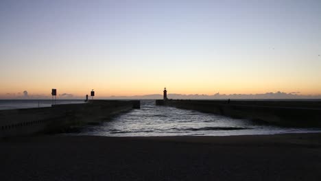 Cold-sunset-in-Porto-in-front-of-the-lighthouse,-ocean-tide-and-waves-coming-in-on-a-small-beach,-dark-sunlight
