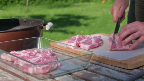 Male-hands-slice-pork-meat-with-chef´s-knife-by-the-grill-in-home-garden