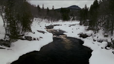 Aerial-scenic-drone-backward-motion-Canadian-wilderness-mid-winter-near-north-Quebec-Stoneham-Ski-Resort-of-frozen-over-Sautaurski-River-down-stream