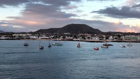 aerial-sunset-view-of-Corralejo-town-on-the-northeast-coast-of-Fuerteventura,-one-of-the-Canary-Islands-of-Spain-dramatic-sunset-with-sail-boat-moored-at-bay