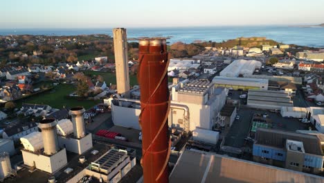 Backwards-reveal-from-power-station-chimney-revealing-industrial-area,-harbour-covering-area-from-Leale’s-Yard-to-Vale-Castle-and-sea-beyond,-St-Sampson-Guernsey-in-late-afternoon-sun