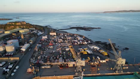 Drone-flight-over-the-docks-St-Sampsons-Harbour-Guernsey-showing-cargo-ship,-cranes,-yards-and-industry-flying-out-to-sea-and-ancient-castle-with-views-of-the-Islands