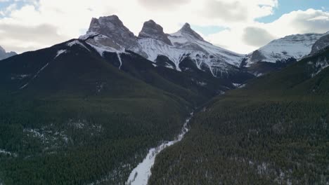 Aerial-view-of-Three-Sisters-mountain-peak-with-valley-and-forest,-Alberta,-Canada---Drone-4k
