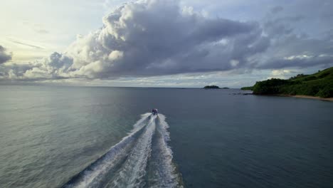 Boat-cruising-towards-cloudy-horizon-along-the-coast,-Yasawa-islands,-Fiji