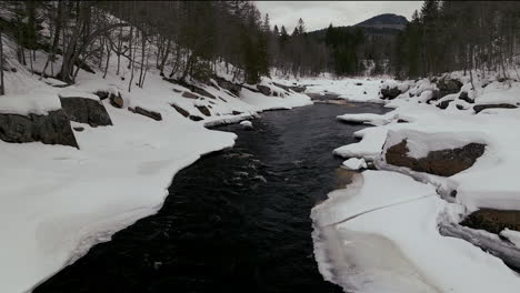 Aerial-scenic-drone-forward-reveal-motion-Canadian-wilderness-mid-winter-near-north-Quebec-Stoneham-Ski-Resort-of-frozen-over-Sautaurski-River-upstream