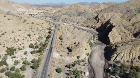 Aerial-drone-zoom-in-shot-over-a-vehicle-parked-alongside-a-winding-RCD-Road-surrounded-by-arid-vegetation-in-Balochistan-at-daytime