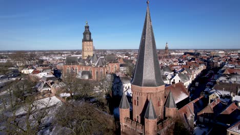 Aerial-approach-and-passing-of-Drogenapstoren-in-tower-town-Zutphen-towards-Walburgiskerk-cathedral-with-small-historic-Dutch-city-covered-in-snow-in-The-Netherlands-and-river-IJssel-passing-by-behind