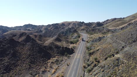 Aerial-drone-following-shot-over-truck-driving-along-winding-RCD-Road-surrounded-by-mountain-range-in-Balochistan